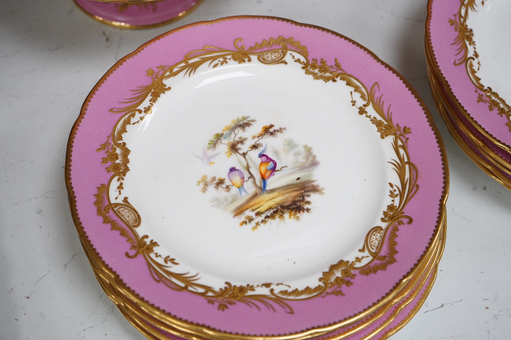 A Minton pink ground dessert service, in Sevres style, c.1850, hand painted with birds, comprising four comports and ten dessert plates, 23cm in diameter